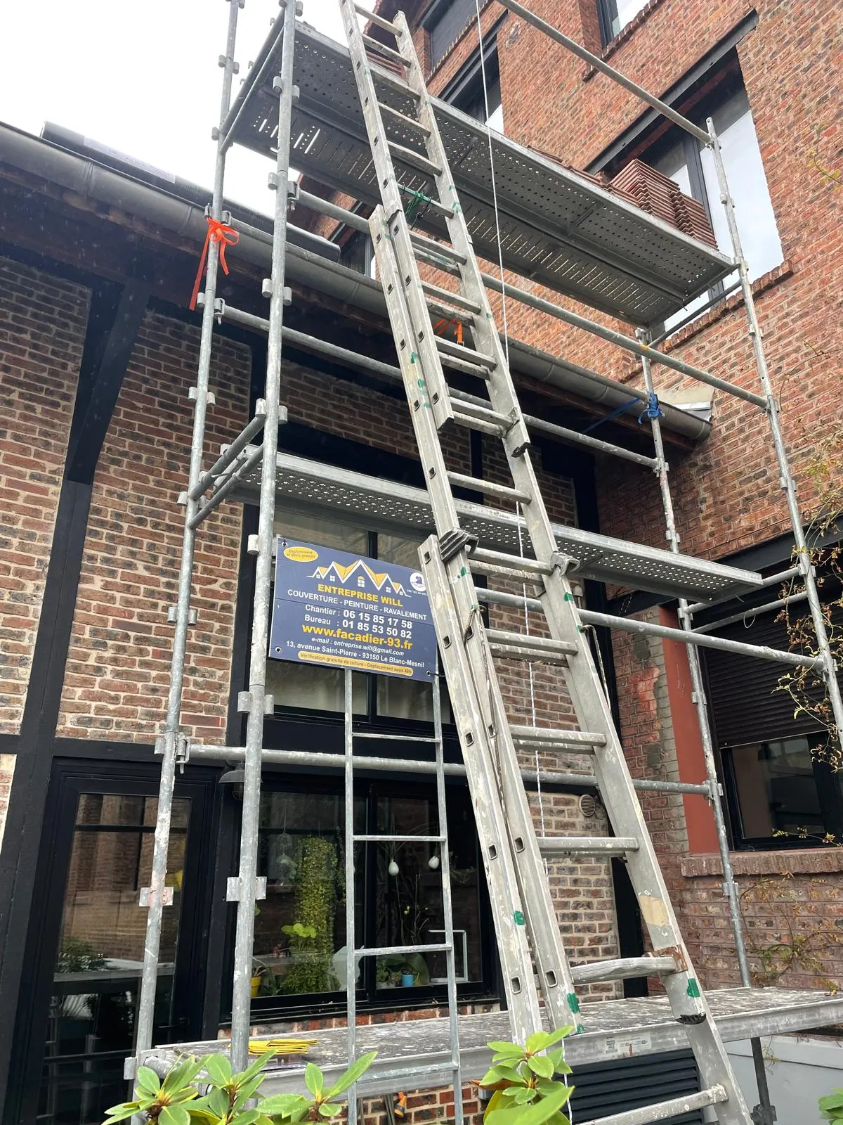 Couvreurs montant les tuiles sur le plateau d’un échafaudage devant un pavillon en brique — chantier Will Couvreur