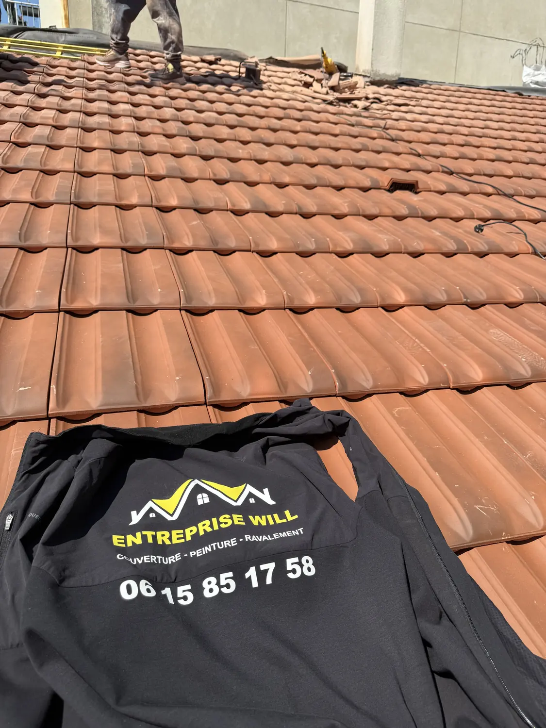 Veste de travail floquée au nom de l’entreprise, posée sur une couverture en tuiles neuves